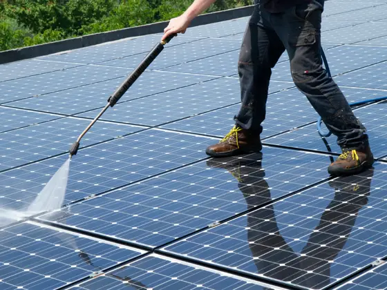 A rooftop solar array being rinsed clean with a spray wand